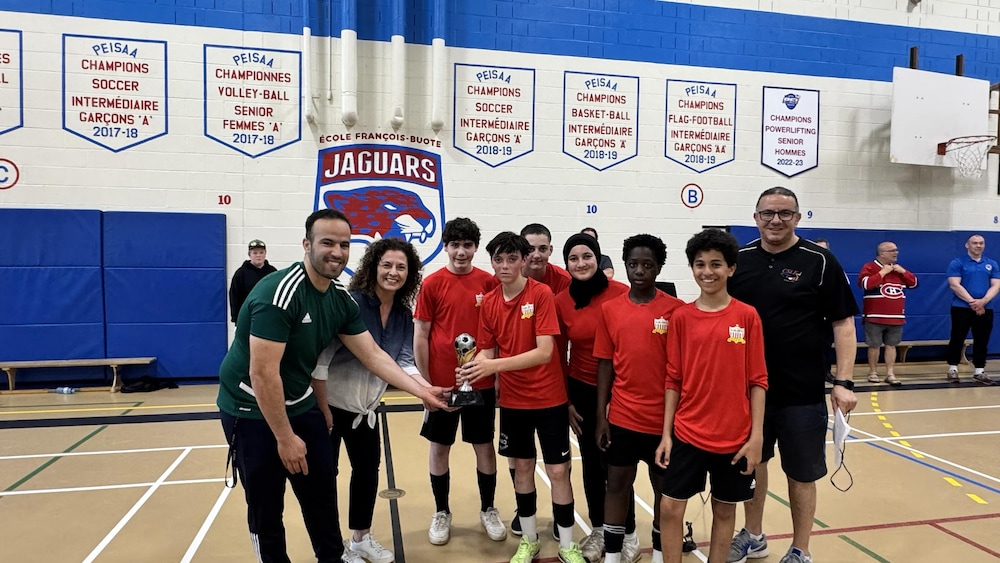 Des élèves et des enseignants avec un trophée dans un gymnase d'école.