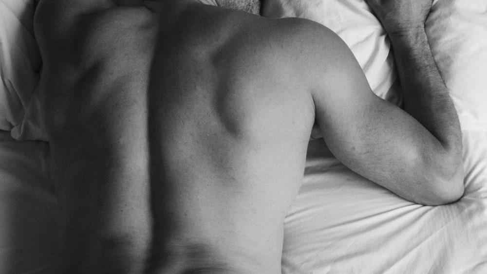 Photo en noir et blanc d'un homme étendu sur le ventre dans un lit, le dos dénudé.