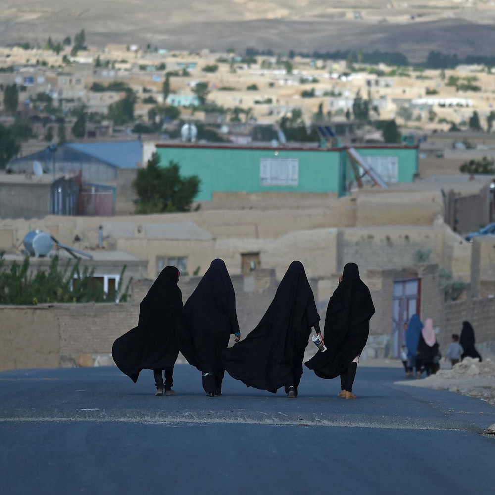 Quatre Afghanes vues de dos marchent au milieu d'une rue dans la ville de Ghazni en Afghanistan.