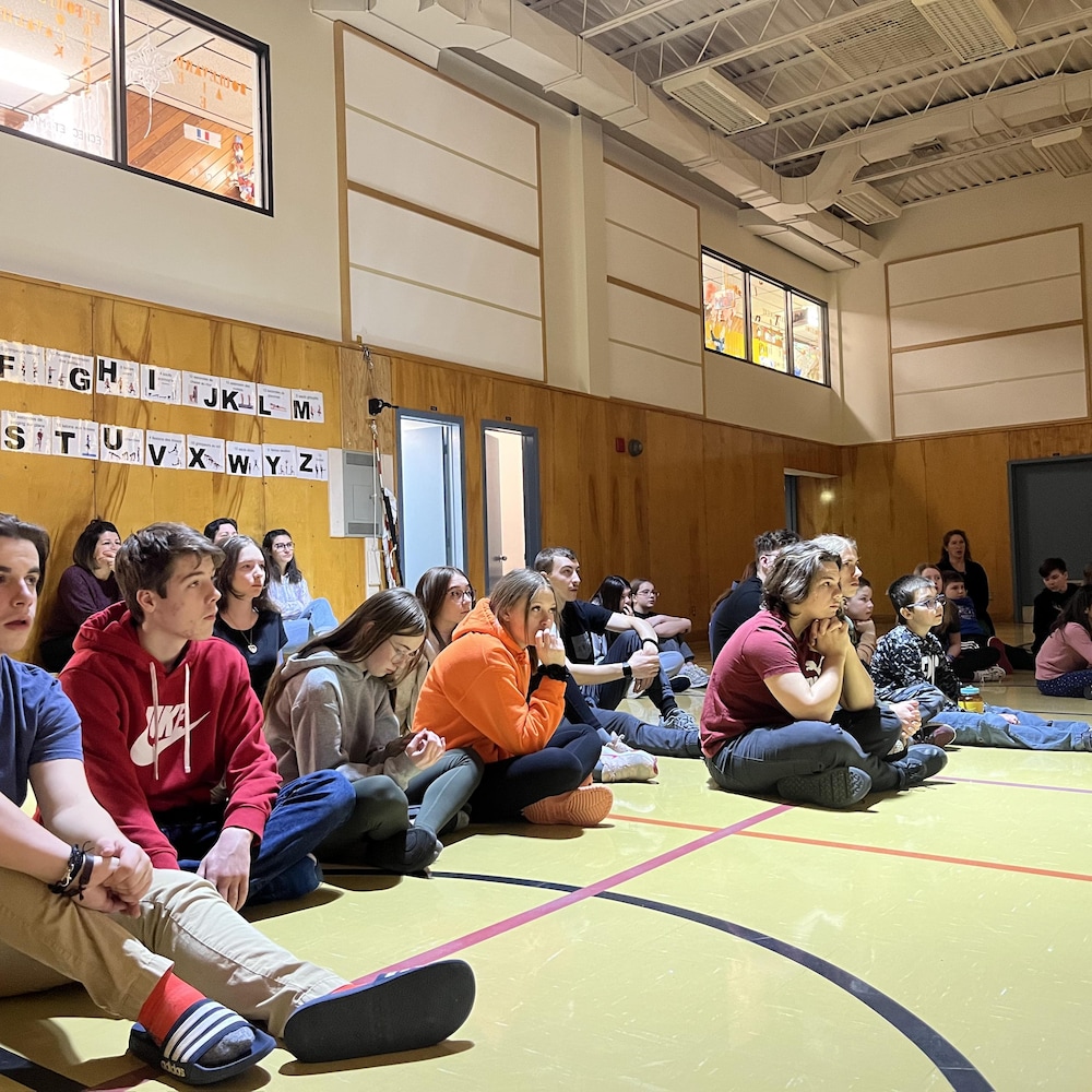 Un groupe d'élèves assis par terre dans le gymnase.