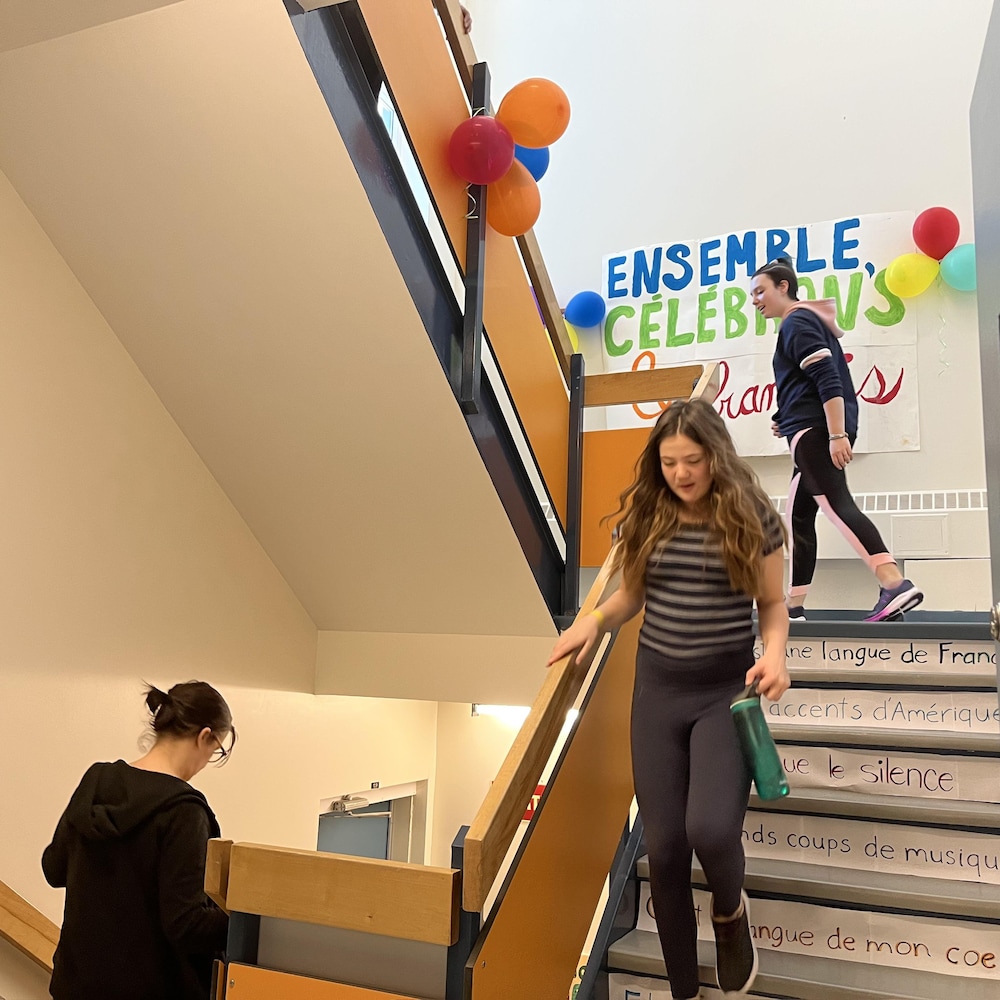 Des élèves dans un escalier décoré par une affiche où on peut lire Ensemble célébrons le français.