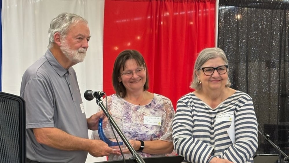 Un homme recevant son prix des mains de deux femmes.