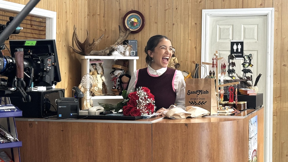 Une jeune femme qui rit derrière un comptoir d'un magasin sur un plateau de tournage.