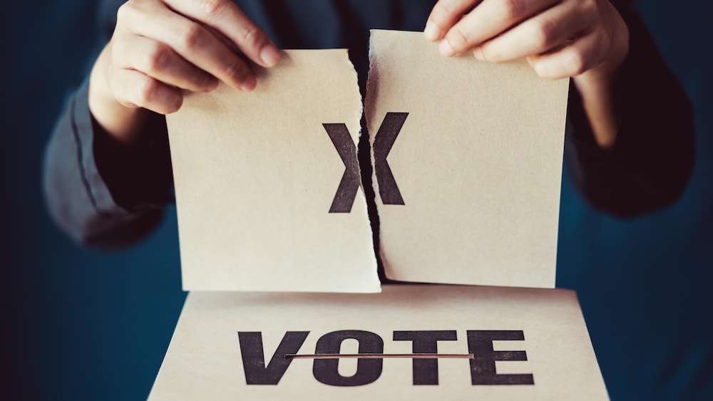 Une personne qui tient un bulletin de vote déchiré en deux parties.