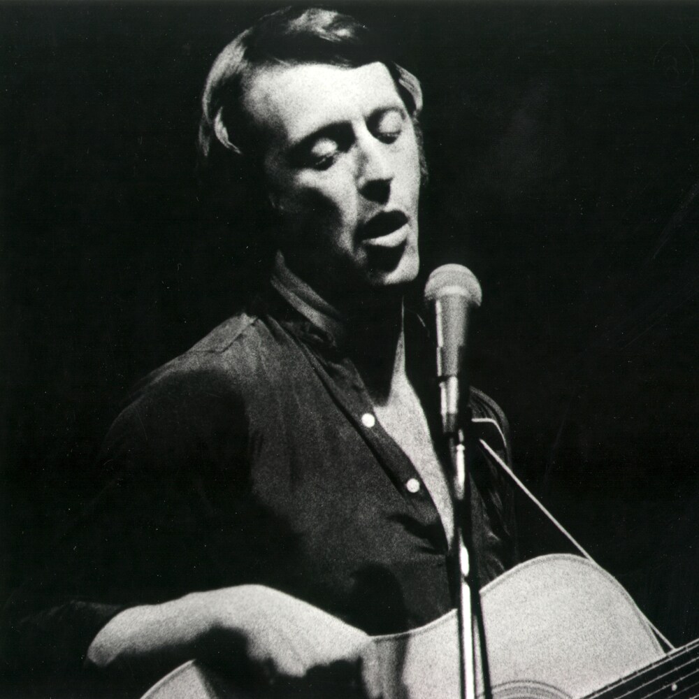 Marcel Aymar avec une guitare devant un micro.