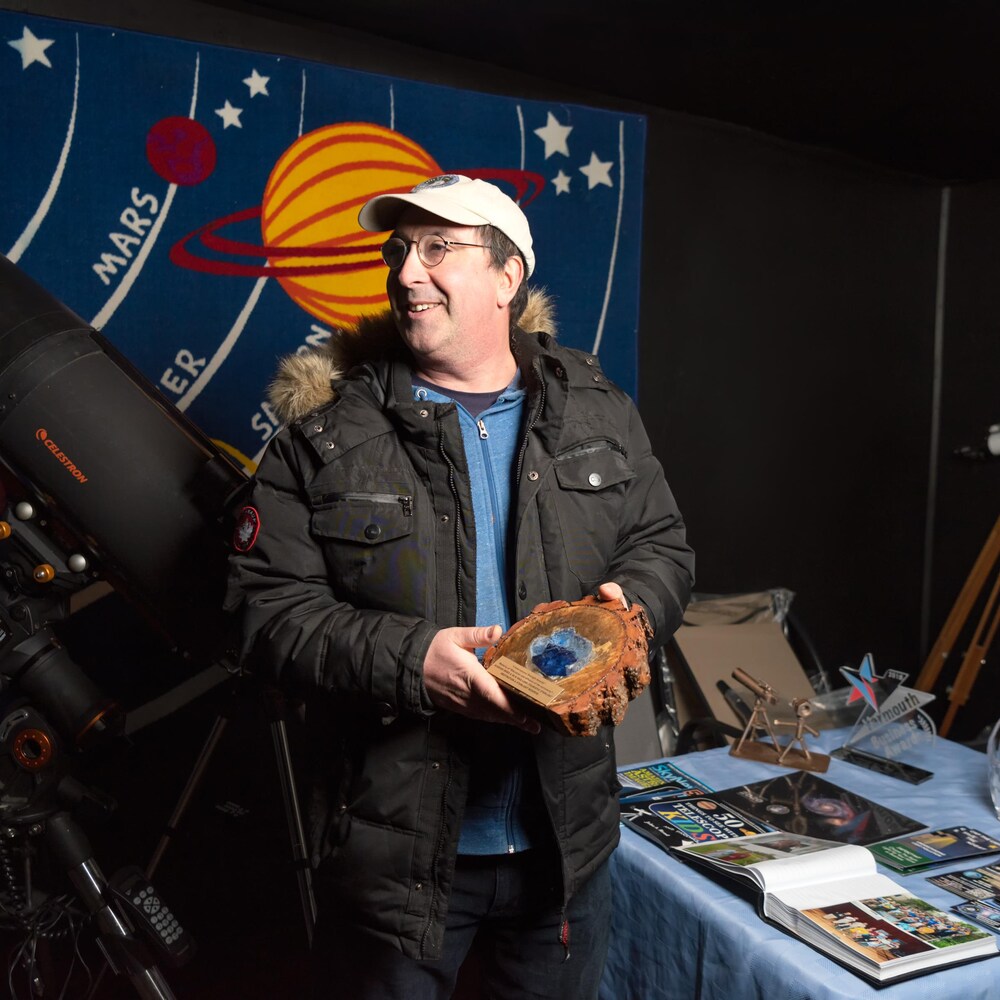 Tim Doucette debout dans son observatoire tient un trophée.