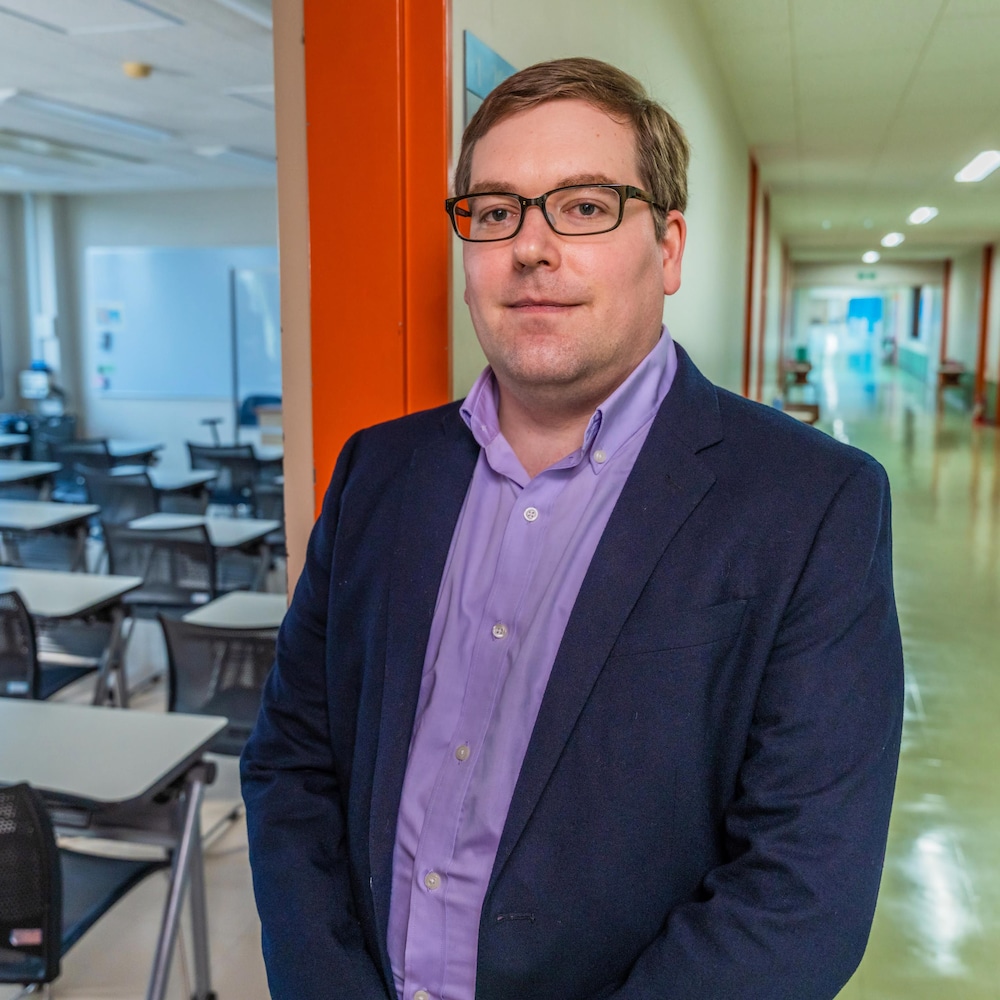 Un homme debout dans un cadre de porte entre une classe et un corridor d'une école.