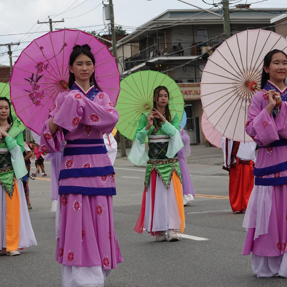 Des personnes en costumes traditionnels chinois marchent avec des ombrelles.