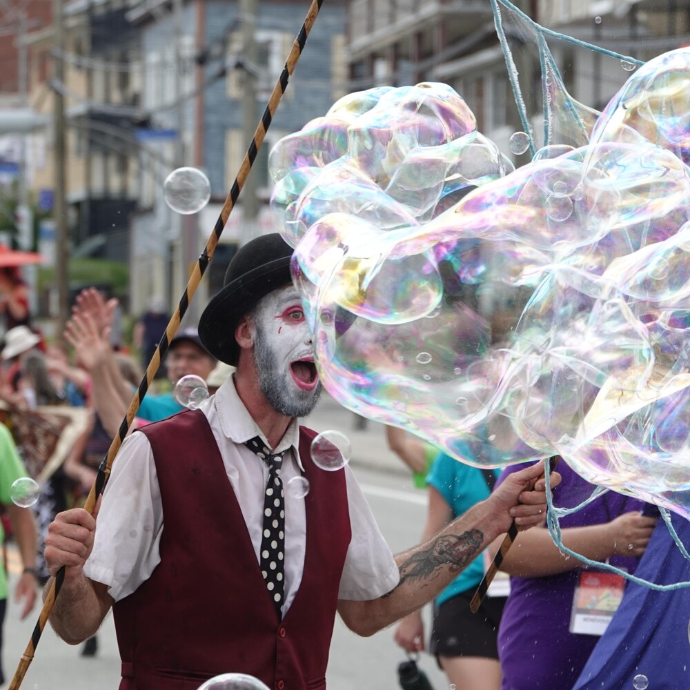 Une personne avec un maquillage de clown fait des bulles.