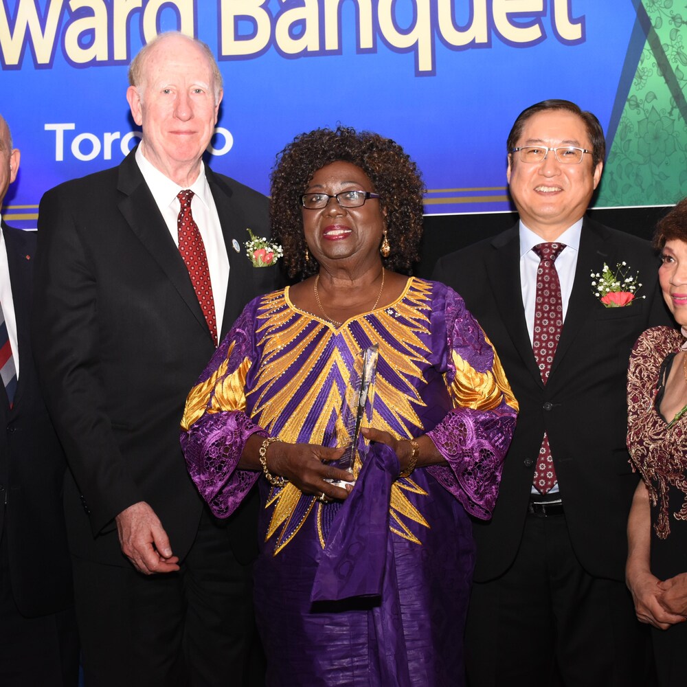 Jean Augustine (au centre) tient un trophée de verre entourée de quatre personnes.
