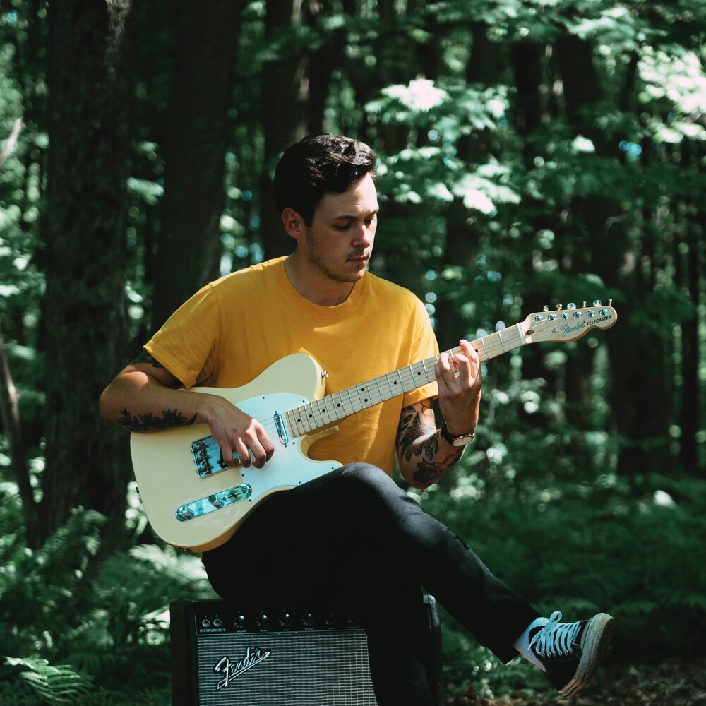 Tristan Guay joue de la guitare dans une forêt.