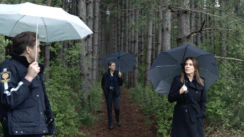 Deux femmes et un homme dans la forêt. Ils tiennent des parapluies.
