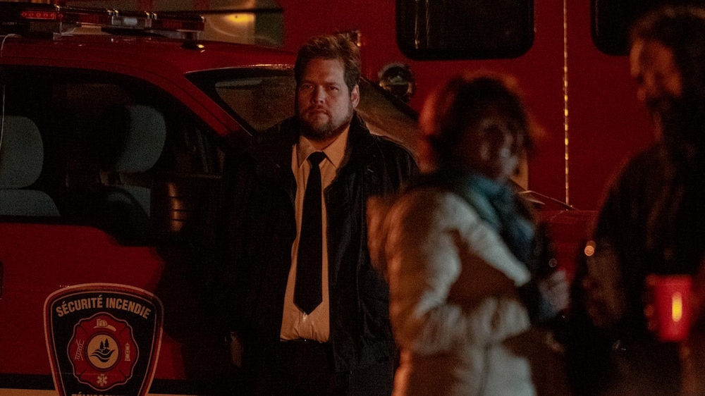Sphere Films Un homme (Guillaume Cyr) en uniforme, devant un camion de pompier, au milieu d'une foule.