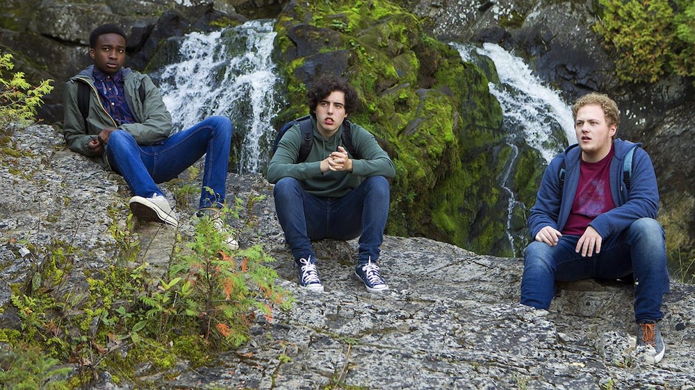 Trois jeunes hommes assis sur des roches.