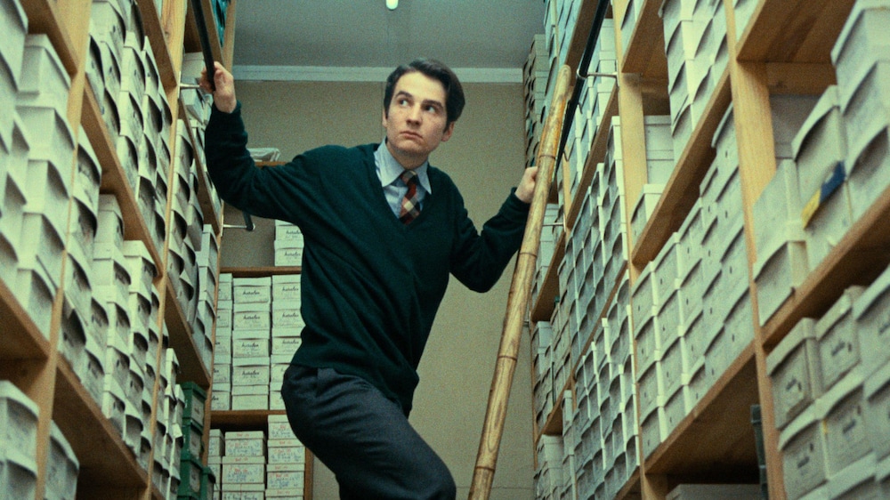 Un homme (Jean-Pierre Léaud) sur une échelle entre des étagères pleines de boîtes.