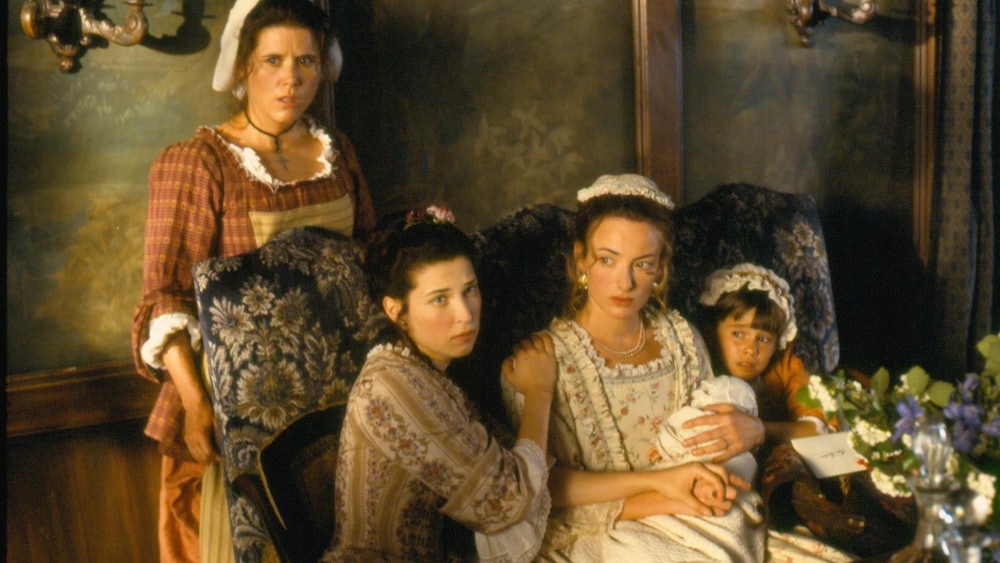 Radio-Canada Deux femmes habillées avec des vêtements d'époque sont assises avec deux enfants et une autre femme est debout derrière elles.