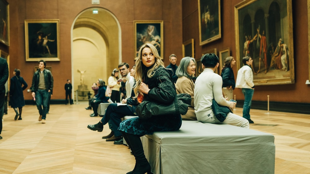 Radio-Canada / Caroline Dubois Sylia est assise dans une salle remplie de tableaux au Musée du Louvre.