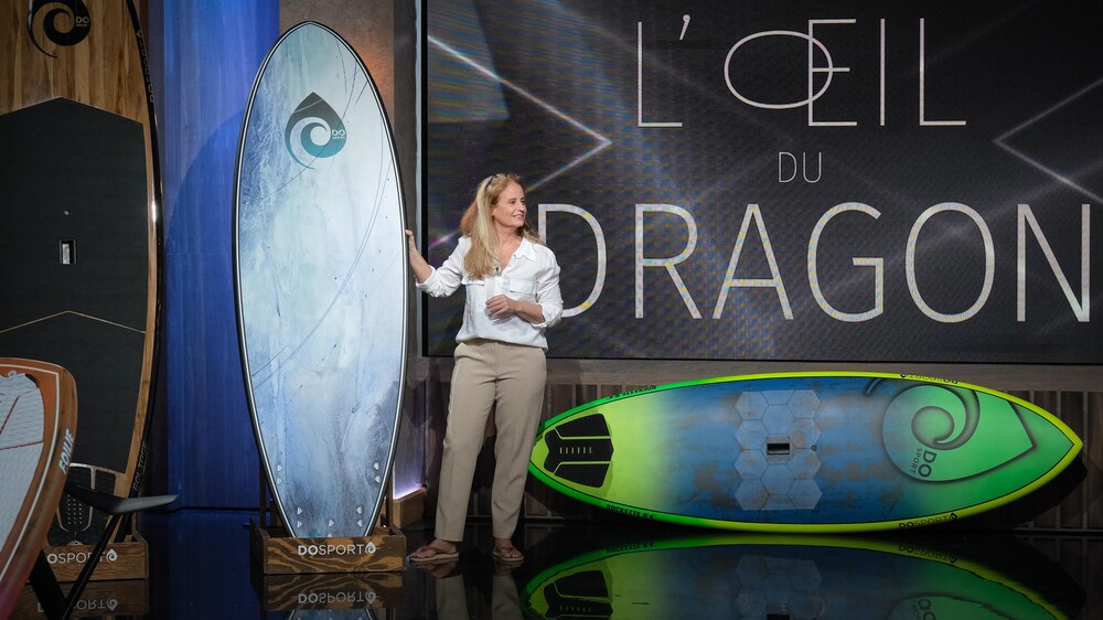 Une femme présente son entreprise. Elle se tient à côté d'une planche nautique.