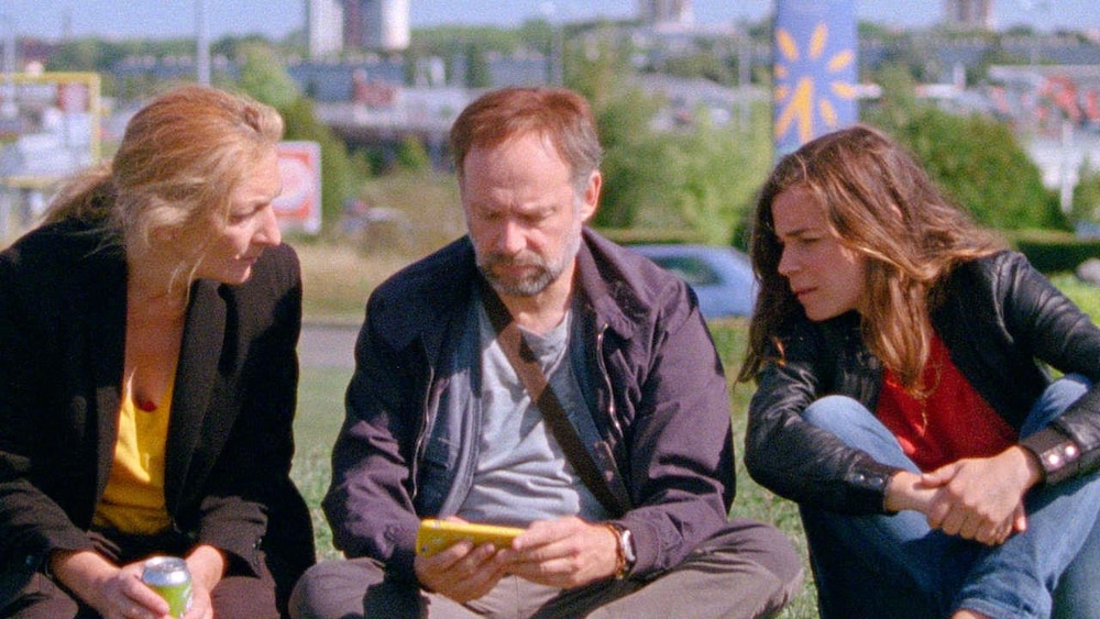 Métropole Films Deux femmes (Corinne Masiero et Blanche Gardin) assises autour d'un homme (Denys Podalydès) regardent le téléphone qu'il tient dans les mains.