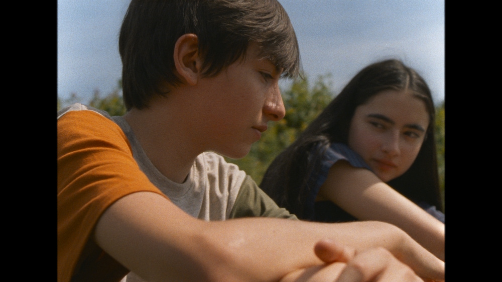 Sphere Films Un jeune homme et une jeune fille assis dehors.