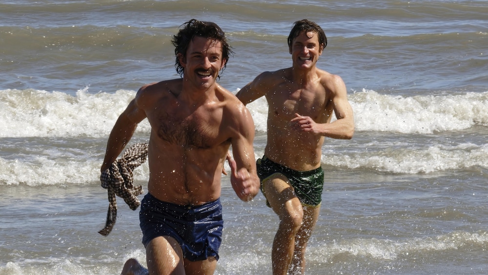 Tim Laughlin et Matt Bomer courent sur une plage, le sourire aux lèvres. 