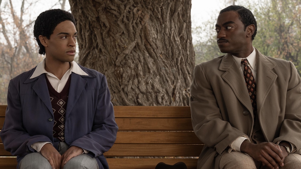 Frankie et Marcus sont assis aux opposés sur un banc dans un parc et se regardent. 