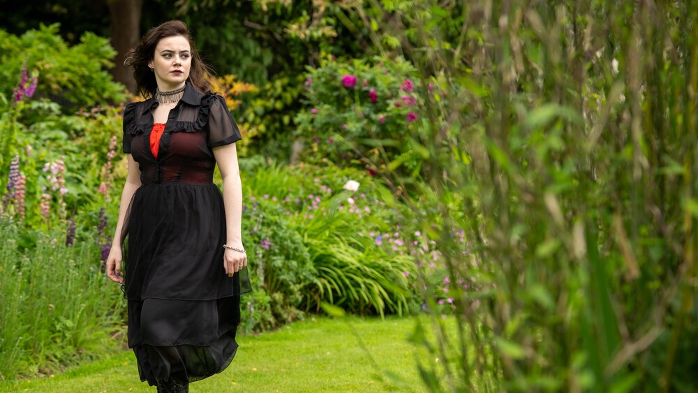 Une jeune femme au style gothique inquiète dans un jardin.