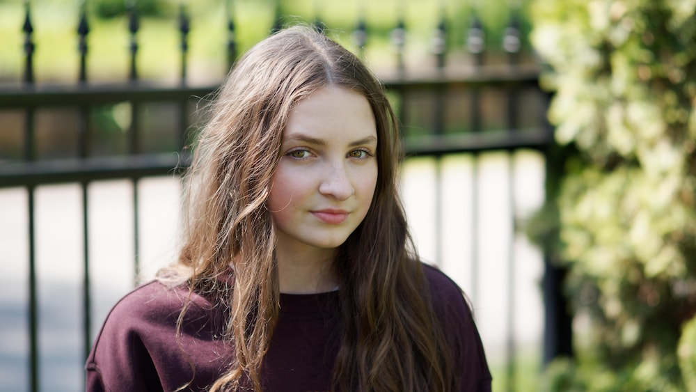 Les Productions Sovimage Une jeune femme qui regarde la caméra. Elle est dehors, devant une clôture en fer forgé.