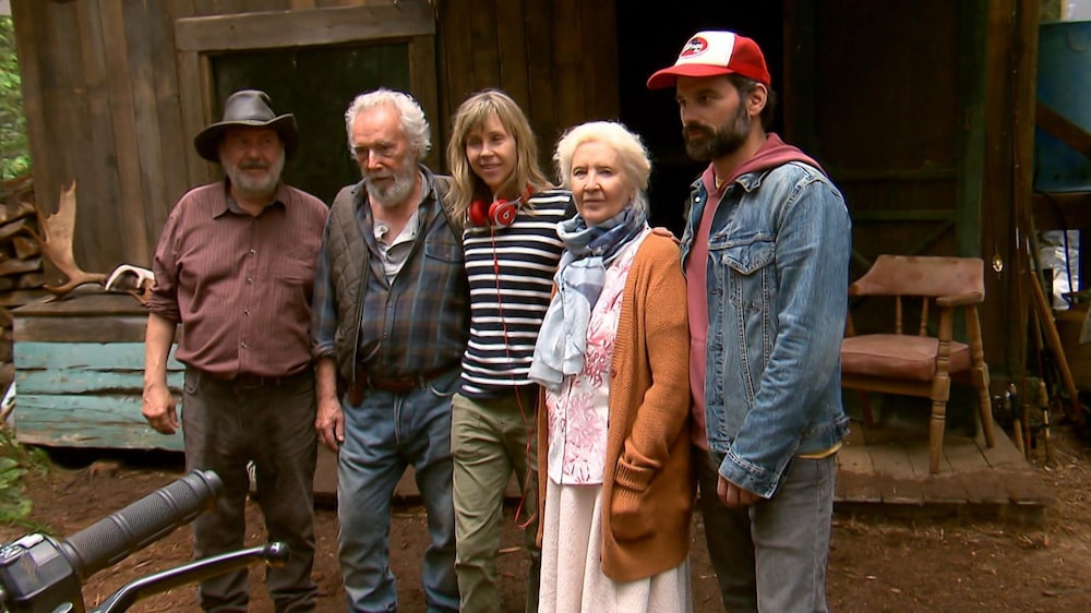 Radio-Canada 5 personnes sont côte à côte devant une cabane délabrée dans la forêt.
