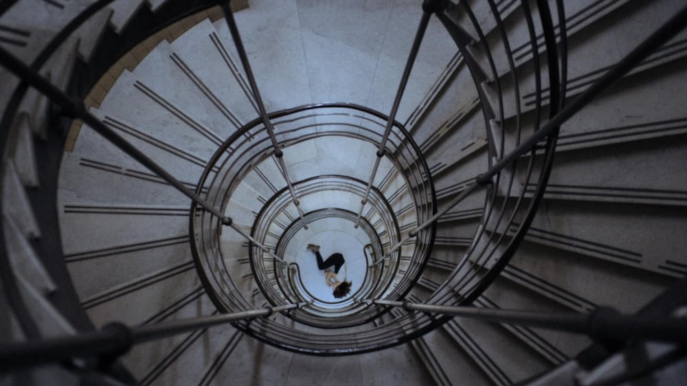 Une jeune femme allongée vue d'en haut d'un escalier en colimaçons.