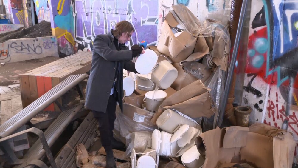 Jean-René Dufort prend des bacs de compost devant une montagne de débris dans un endroit désaffecté plein de béton et de graffitis.