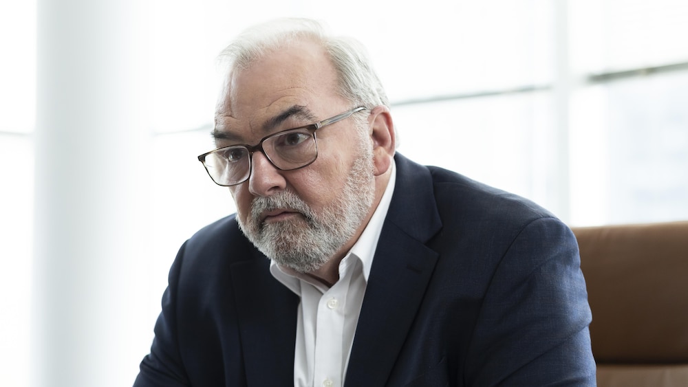 Jean Dumas est assis sur une chaise dans lad   bureau. Il semble perdu dans ses pensées.