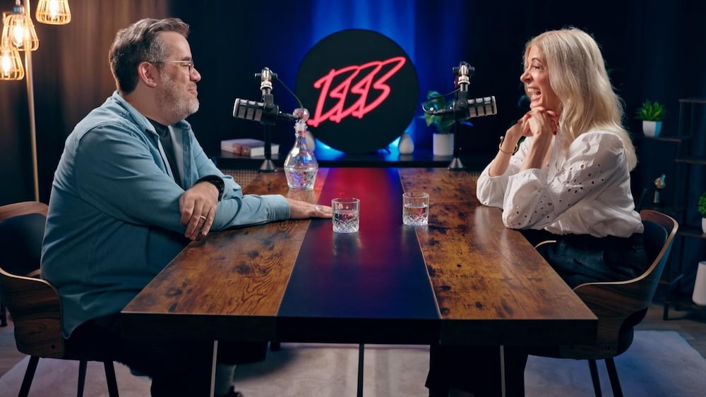 Radio-Canada Assis à une table, Jean-Sébastien Girard regarde Anne-Marie Cadieux qui rit.