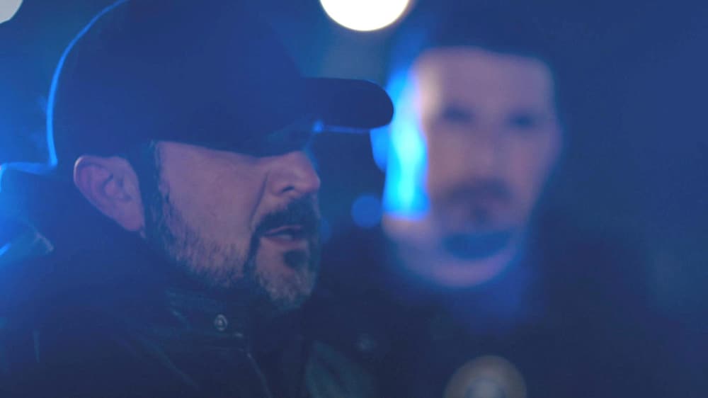 Aetios Productions Joël Jolicoeur (Philippe Dandenault) dehors le soir. Un policier est à côté de lui.