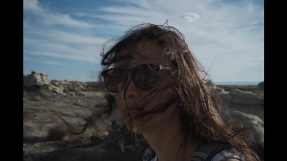 Une jeune femme, les cheveux dans le vent, dans un désert.