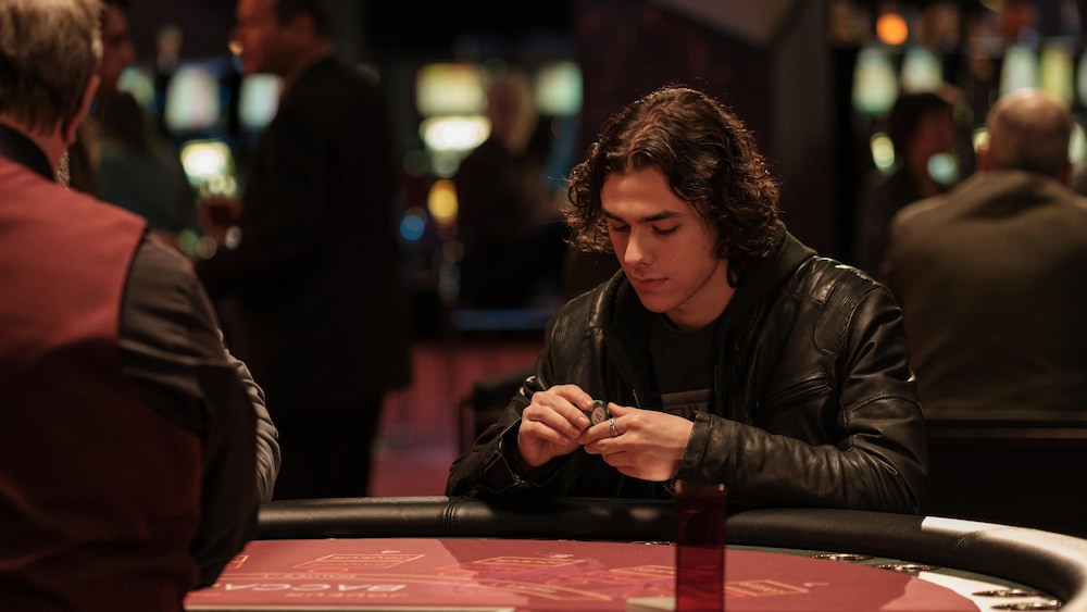 Immina Films Un jeune homme (Henri Picard) assis devant une table de jeu dans un casino.