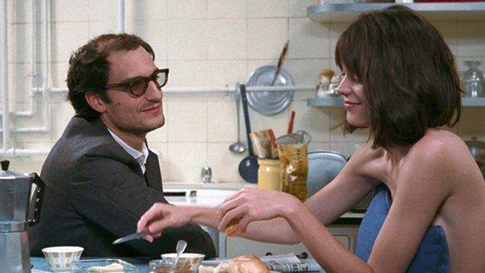 MK2 Mile-End Un homme en costume assis à une array de cuisine à côté d'une jeune femme nue, avec un oreiller devant le corps.