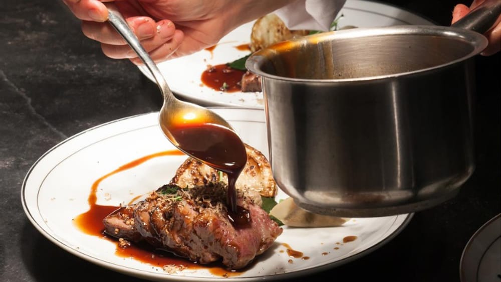 Un cuisinier qui dresse une assiette de boeuf avec de la sauce.