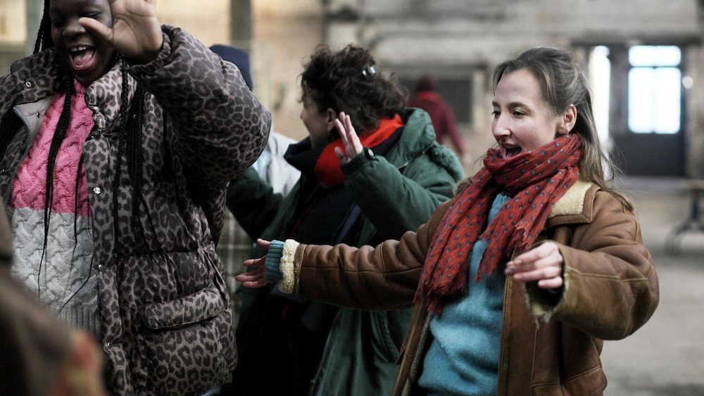 Plusieurs femmes dansent, dehors, chaudement vêtues.