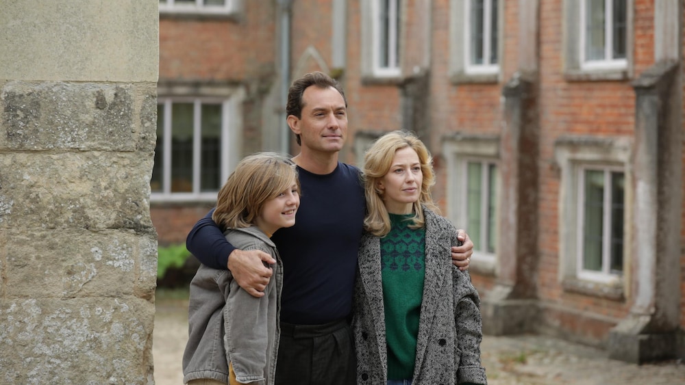 Dans une cour, un homme tient par les épaules une femme et un garçon.