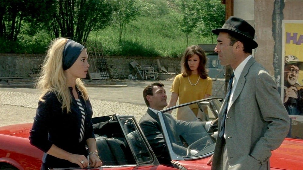 Studio Canal Un homme (Michel Piccoli) et une femme (Brigitte Bardot) discutent debout devant une voiture.