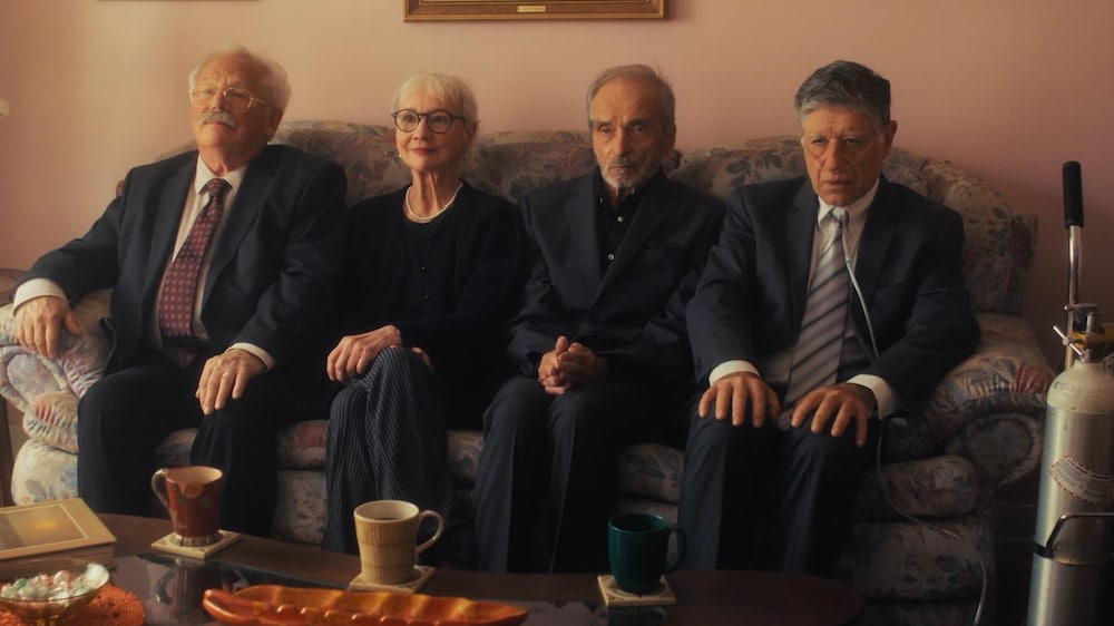 Trois hommes et une femme sont assis sur un sofa.