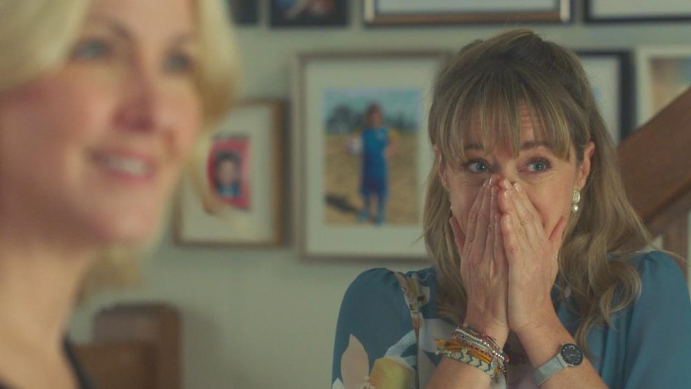 Isabelle met ses mains devant sa bouche et son nez, l'air content.