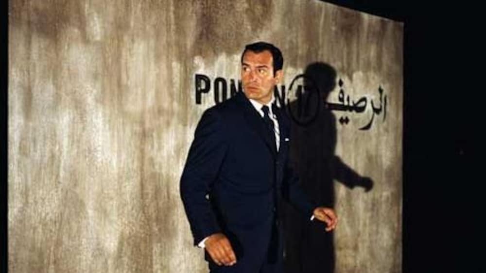 Un homme devant un mur où apparaissent des mots en français et en arabe.
