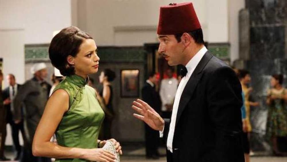 Un homme avec un fès sur la tête parle à une femme en robe verte.