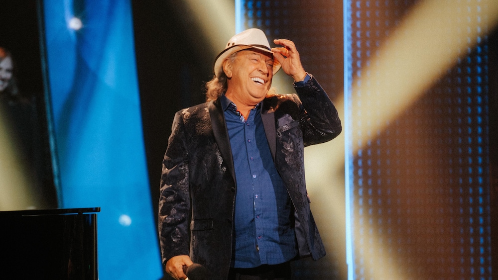 Le chanteur country est sur scène et tient son chapeau de cowboy en souriant.