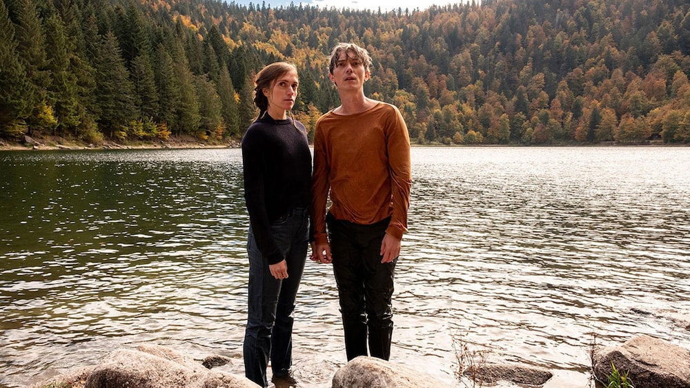 Pascal Chantier Un homme et une femme debout, les pieds dans un lac.