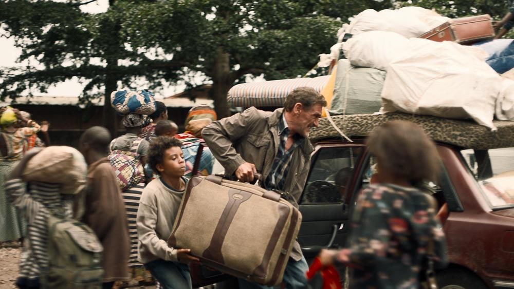 AZ Films Un homme suivi d'un jeune garçon portent une grosse valise vers une voiture.