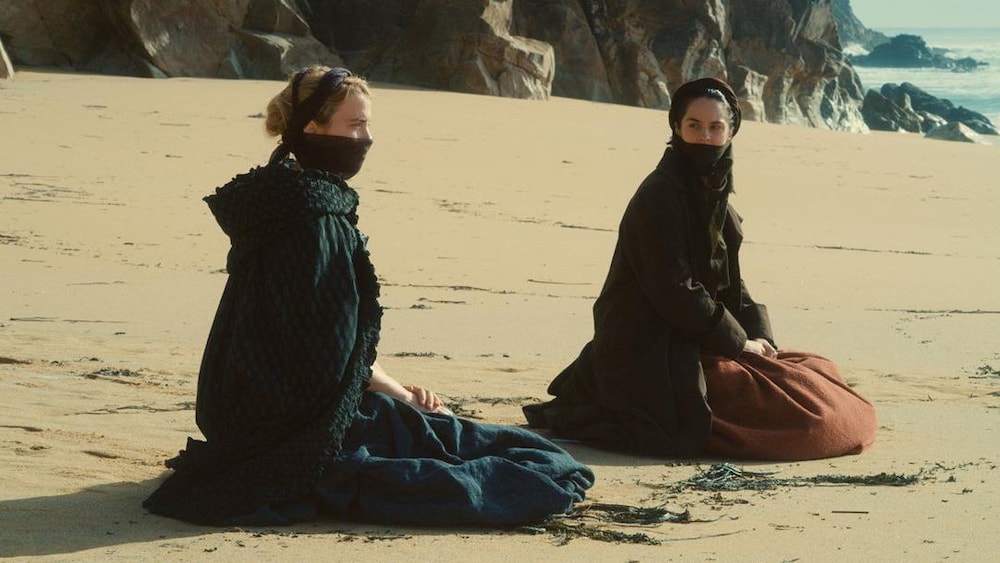 Deux jeunes femmes assises dans le sable, sur une plage.