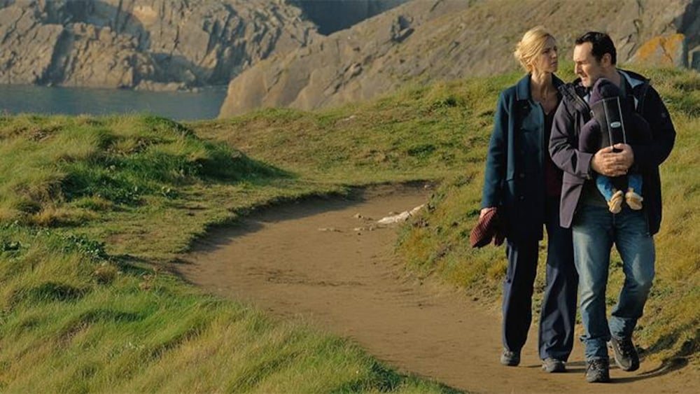 Trésor Films Une femme (Sandrine Kiberlain) et un homme portant un bébé (Gilles Lellouche) marchent le agelong d'une falaise.